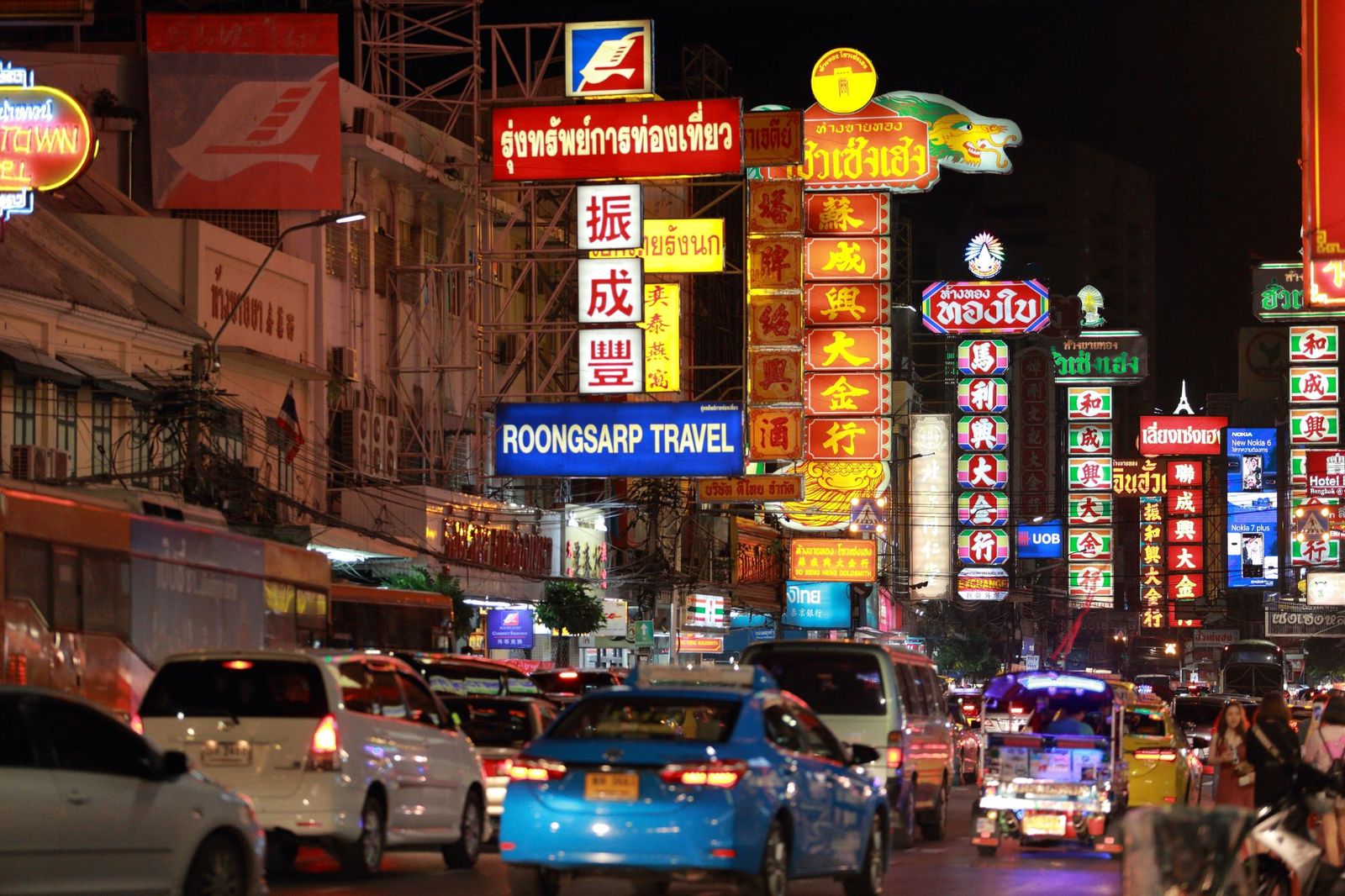 Rows of lit shop signs down both sides of Yaowarat Road at night, traffic backed up in between